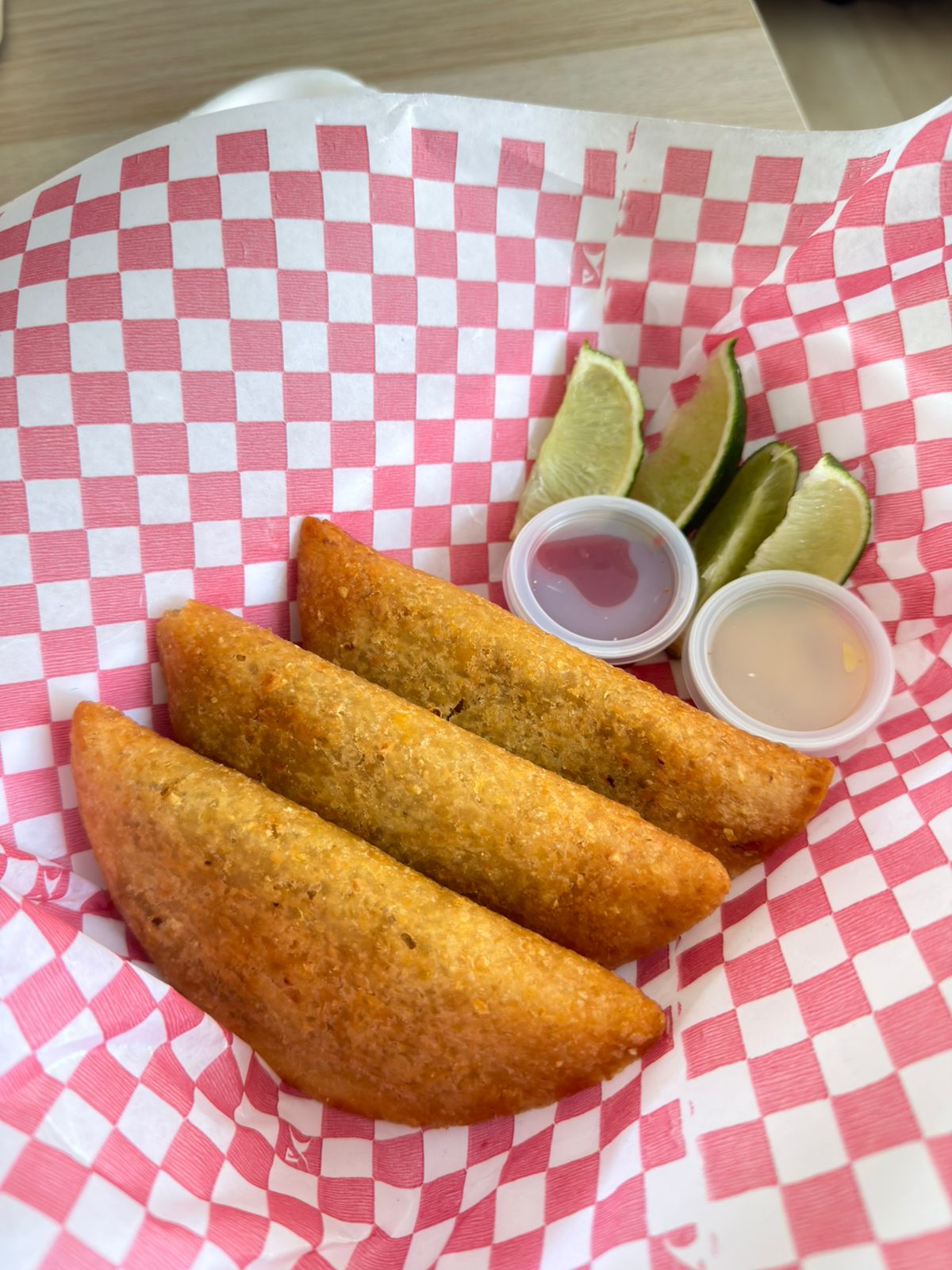 Tres empanadas vallunas de La Caleñita sobre papel de cuadros, con limón y salsas